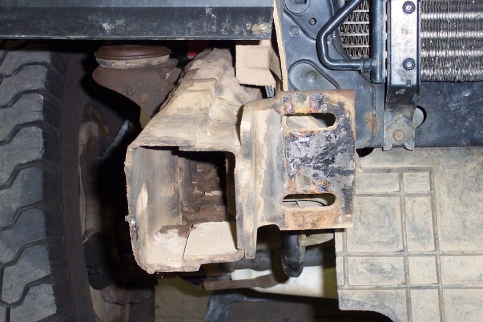 Rusty frame rail and bracket under a vehicle, tire at left, radiator at upper right