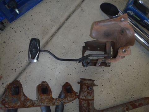 1978 Ford Bronco - Close-up of rusty vehicle parts, including a brake pedal and exhaust manifold, on a garage floor.