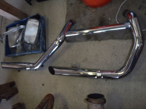 1978 Ford Bronco - Chrome exhaust pipes and side mirrors are laid out on a concrete floor.