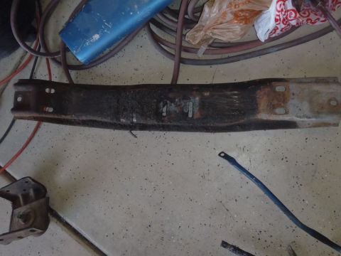 1978 Ford Bronco - A rusty metal part, possibly a crossmember, lies on a concrete floor with various hoses and a plastic bag nearby.