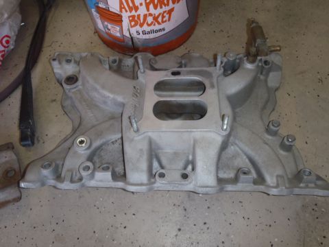 1978 Ford Bronco - Close-up of an aluminum intake manifold with a brass fitting, resting on a concrete floor.