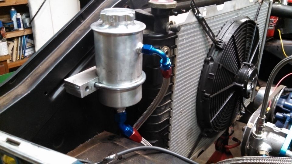Close-up of a power steering reservoir mounted next to a radiator and electric fan