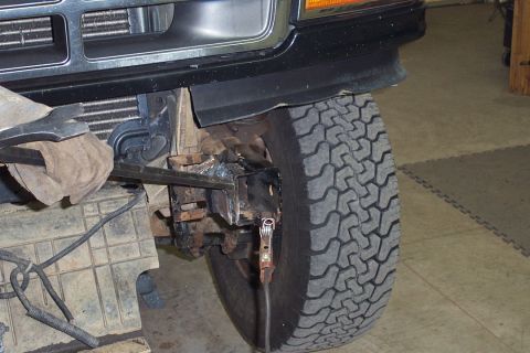 1996 Ford Bronco - Close-up of the front driver-side suspension and steering components on a dark-colored Ford Bronco, showing the wheel hub area, tie rod/rad…