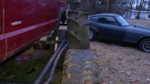 1978 Ford Bronco - A red truck and a dark sports car are parked outdoors, partially obscured by large tires.