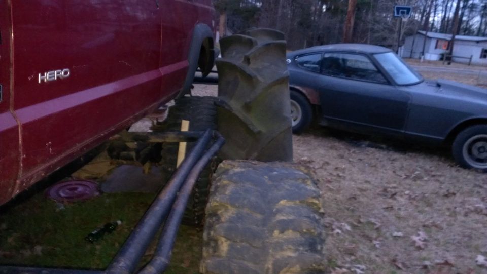 Red truck side view next to dark sports car with large tractor tire in foreground
