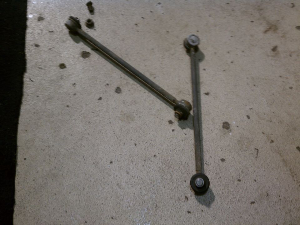 Two metal rods with ball joints on ends, likely suspension components, lying on a concrete floor