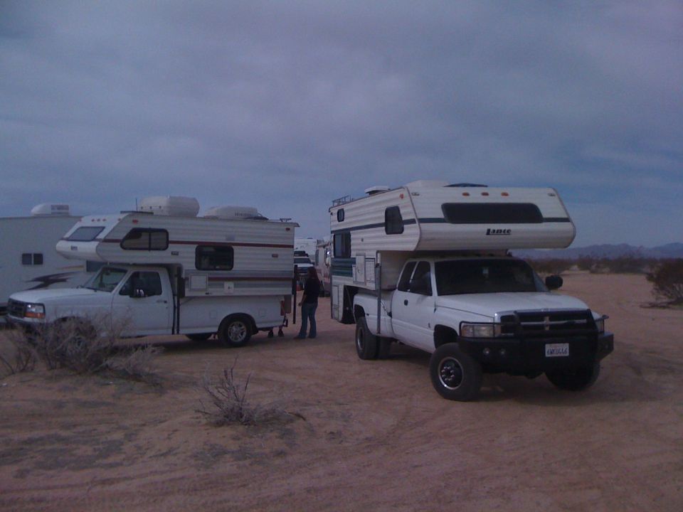 White Ford and Dodge Ram dually pickups with slide-in campers parked on desert sand