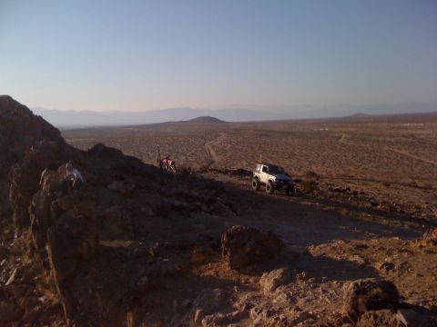 1986 Yugo GV - A white off-road vehicle and a dirt bike are parked on a rocky desert hillside under a clear blue sky.
