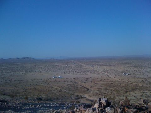 1986 Yugo GV - A wide view of a desert landscape with a dirt road winding through it, dotted with several buildings and vehicles.