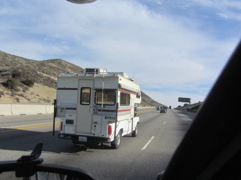 1986 Yugo GV - A white Lance camper is mounted on a white pickup truck driving on a highway.