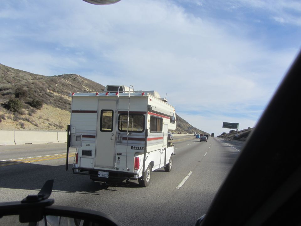 White Lance camper on a white pickup truck, seen from behind on a highway