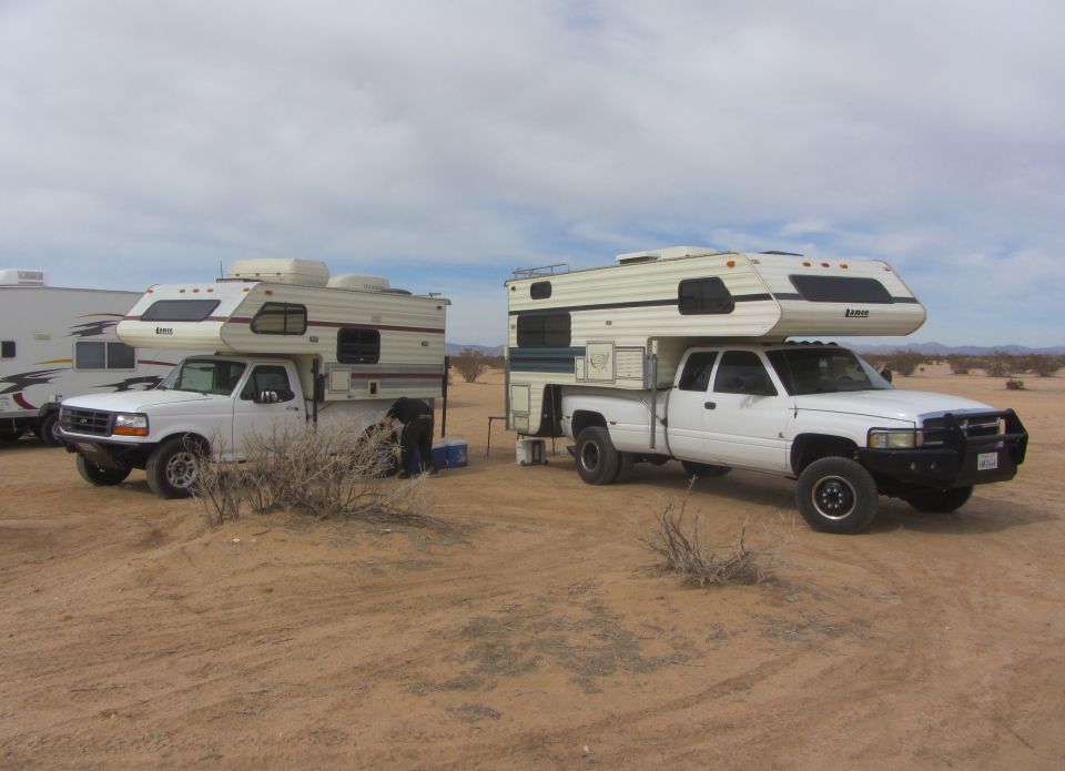 Two white pickup trucks with camper shells parked in a desert landscape