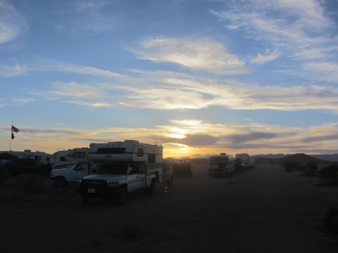 1986 Yugo GV - A desert campsite is set up with multiple vehicles under a cloudy sky at dusk.