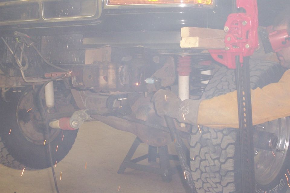 Person grinding on underside of a lifted 4x4, sparks flying near coil springs and shocks