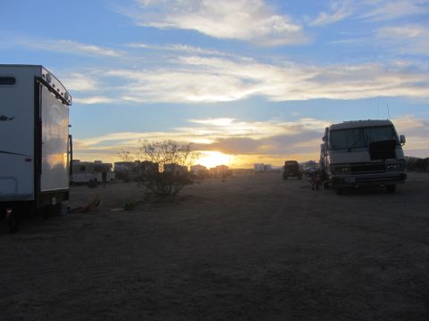 1986 Yugo GV - Several recreational vehicles are parked in a desert setting as the sun sets, casting long shadows.