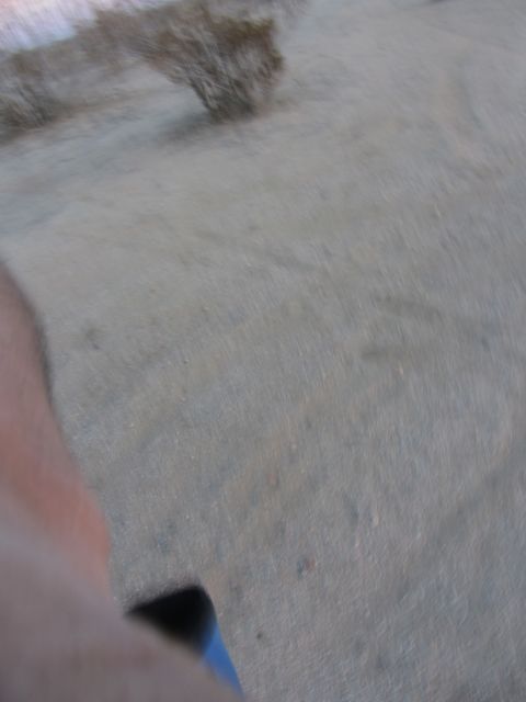 1986 Yugo GV - The image shows a blurry ground surface with some debris and a partial view of a person's arm.