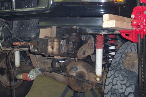 1996 Ford Bronco - Underbody view of a black Ford SUV on jack stands, showing the front solid axle with a red coil spring, white shock absorber, differential…