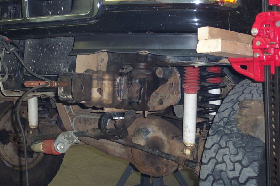 Front axle underside of black SUV with red coil spring and white shock on jack stands