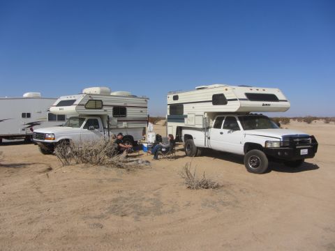 1986 Yugo GV - Two pickup trucks equipped with camper shells are parked in a desert setting under a clear blue sky.