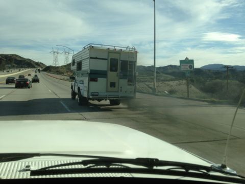 1986 Yugo GV - A truck camper is seen driving on a highway with other vehicles around it under a cloudy sky.