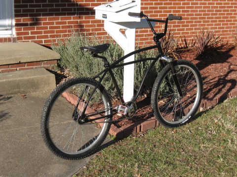 1994 Ford Bronco - A black bicycle with wide tires and handlebars is parked on a lawn next to a mailbox and a brick wall.