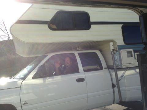 1986 Yugo GV - A white pickup truck is fitted with a camper shell, and the driver waves from the driver's side window.