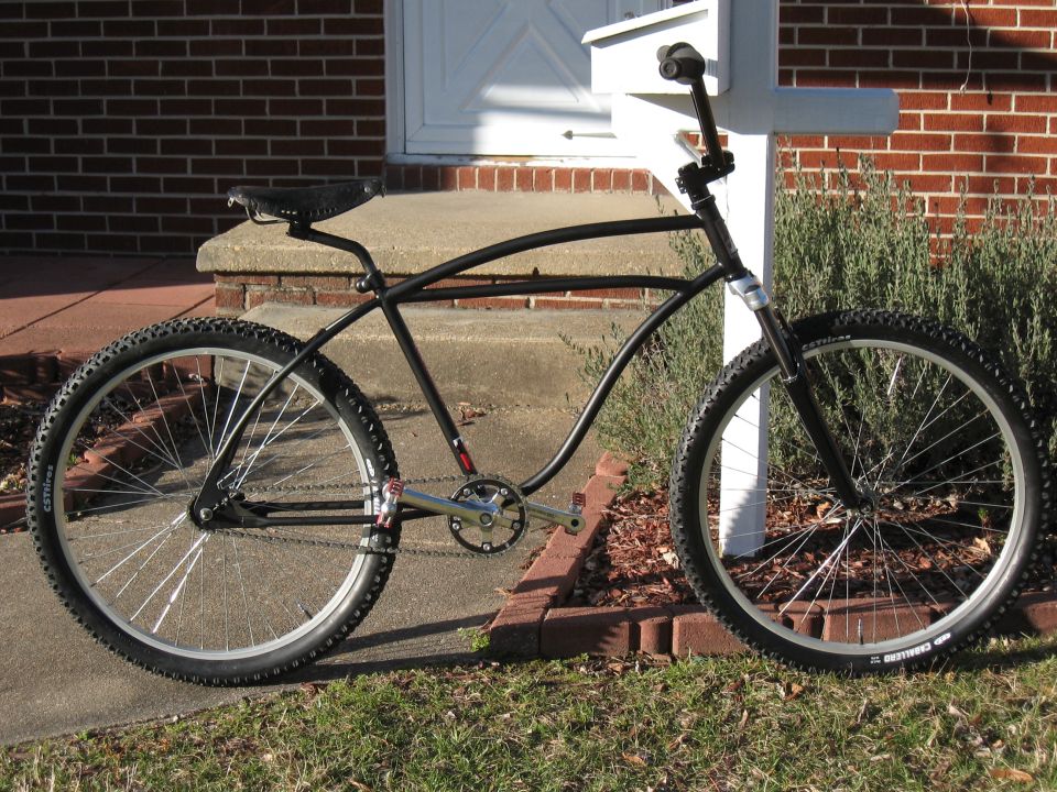 Black custom cruiser bicycle with wide handlebars and knobby tires parked on a sidewalk