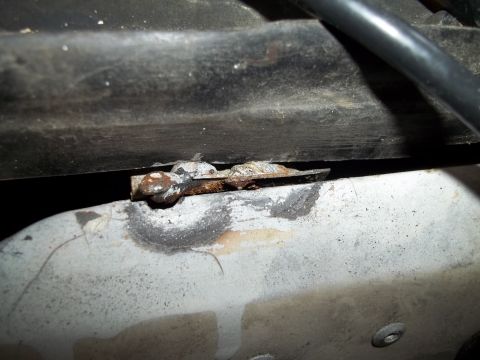 1990 Ford Bronco - Detail of a corroded metal bracket and pipe, likely from a vehicle's undercarriage.