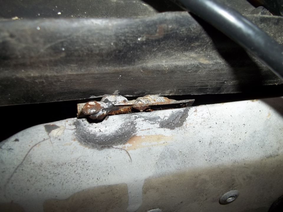 Close-up of a rusted metal bracket attached to a pipe, with a black hose above
