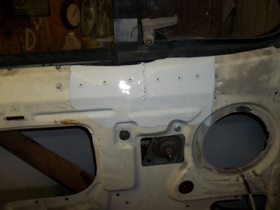 Vehicle firewall with patched section, showing rivets and a circular opening