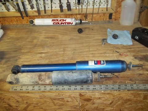 1990 Ford Bronco - Two shock absorbers are laid out on a workbench with a ruler for size comparison.