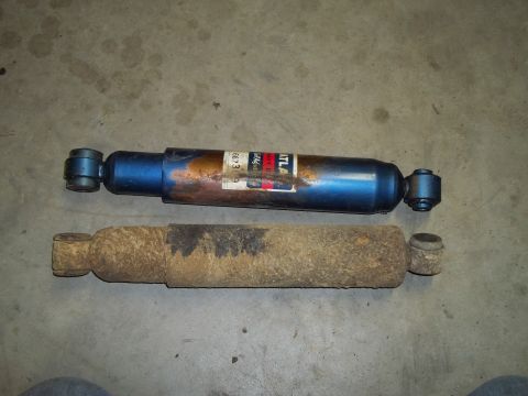 1990 Ford Bronco - A new blue shock absorber is compared to a heavily rusted old one on a garage floor.