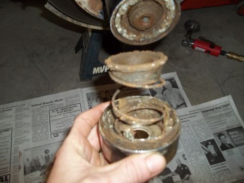 1990 Ford Bronco - A person holds a disassembled, rusty suspension component over newspapers and a jack stand.