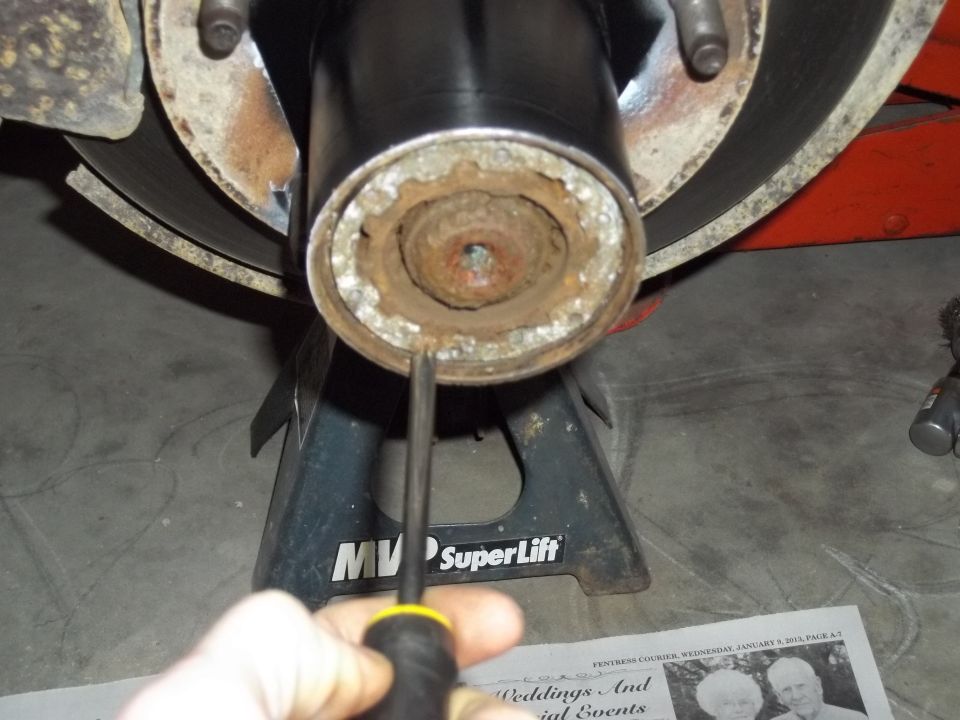 Close-up of a rusty wheel hub assembly on a jack stand, with a screwdriver being used