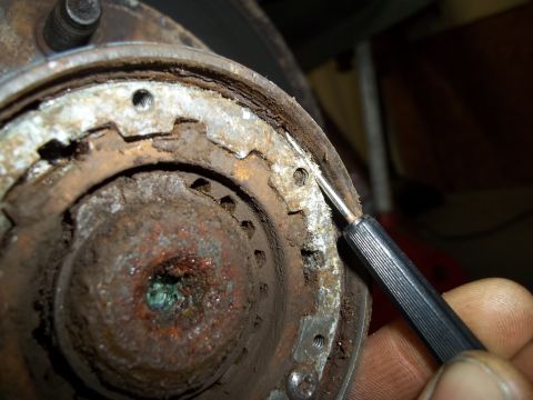 1990 Ford Bronco - Close-up of a rusty brake drum assembly, with a pick tool being used to clean or inspect a part of the components.