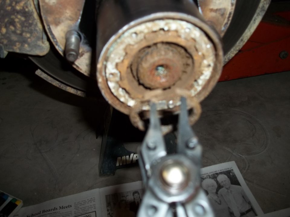 Close-up of a rusty vehicle axle hub with a snap ring being removed by pliers