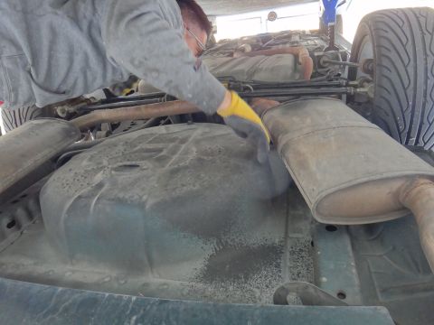 1995 Ford Taurus - Close-up view of a car's underbody, focusing on the fuel tank and exhaust system during maintenance.
