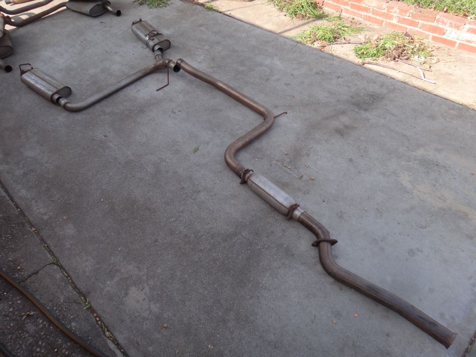 Exhaust system laid out on concrete, showing two mufflers and bent pipes