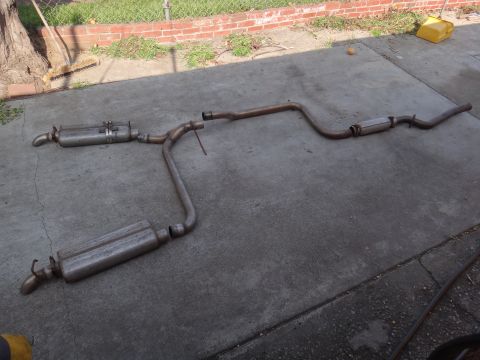 1995 Ford Taurus - A disassembled exhaust system, likely for a car, is shown on a concrete surface.