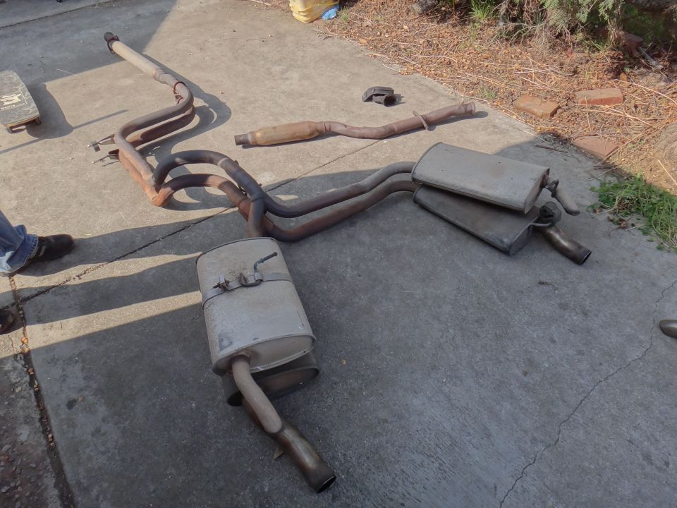 Exhaust system components laid out on concrete, including mufflers and pipes