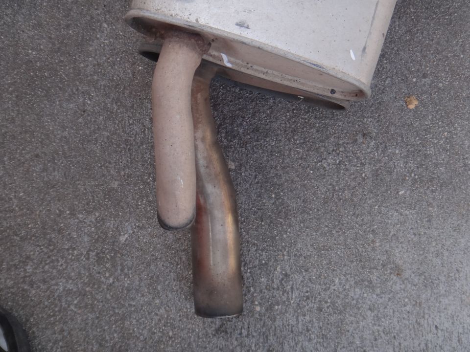 Exhaust muffler with two pipes, one bent and one straight, lying on concrete