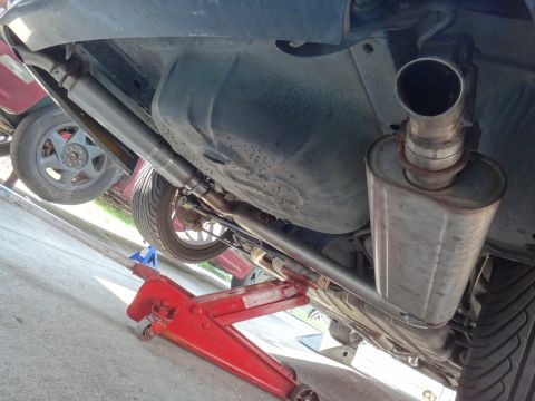 1995 Ford Taurus - The undercarriage of a vehicle is shown, focusing on the exhaust and muffler, with a red jack supporting it.