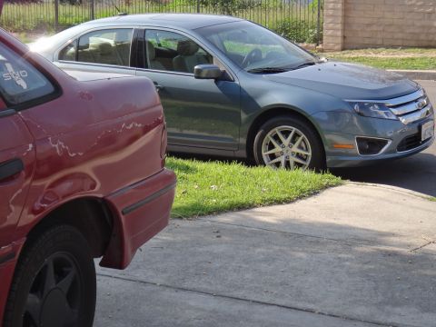 1995 Ford Taurus - A blue sedan is parked on the grass next to a red car on a paved surface.