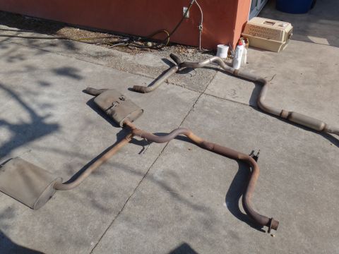 1995 Ford Taurus - Two mufflers and sections of exhaust pipe laid out on a concrete surface.
