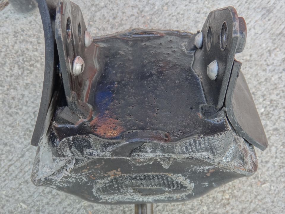 Close-up of a black metal exhaust hanger bracket with visible bolts and wear