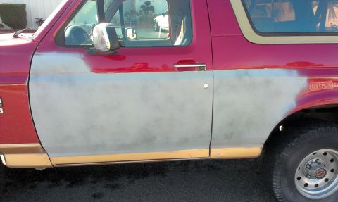 1994 Ford Bronco - Side view of a 1994 Ford Bronco showing primer on the door and fender, with red paint on the upper body.