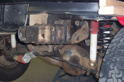 1996 Ford Bronco - Underside view of a 4x4 vehicle's front suspension and axle showing a coil spring, white-bodied shock absorber with red boot, tie rod, and…