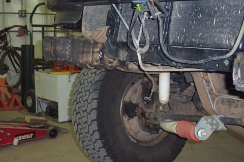 1996 Ford Bronco - Underside rear view of a lifted Ford Bronco showing the rear axle, drum brake backing plate, all-terrain tire, white shock absorber, and a…