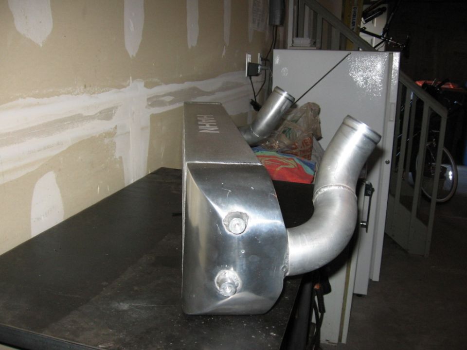 Aluminum intercooler with HAHN branding and two inlet/outlet pipes, resting on a black surface