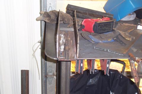1996 Ford Bronco - A workbench in a garage holding fabricated steel brackets or metal parts, with a pair of worn leather work gloves, a red tool, and a blue p…